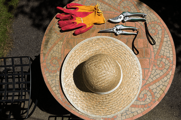 Round table holding a floppy sun hat, a pair of gardening gloves some snips and pruning shears