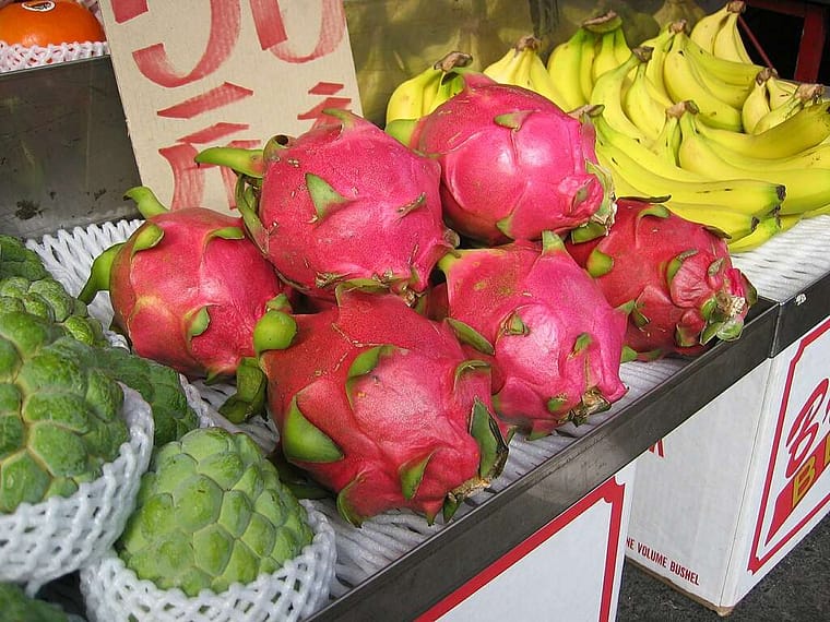 6 red dragon fruit with bananas to their right at a produce stand